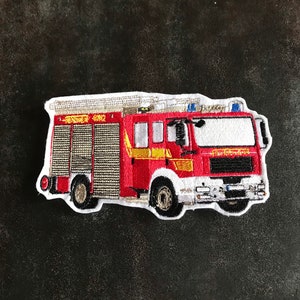Könnte beinhalten: Rotes und weißes gesticktes Patch eines Feuerwehrautos mit dem Text "Feuerwehr 5012" an der Seite.