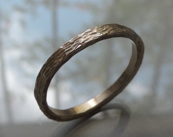May include: A simple, rustic-style wedding band with a textured, bark-like finish. The band is made of a light gold metal.