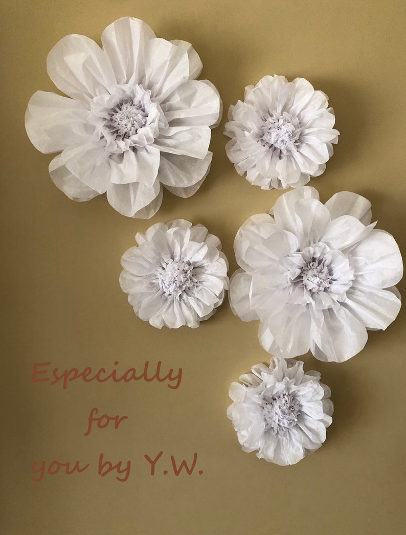 May include: Five white paper flowers of varying sizes are arranged on a beige background. The flowers are made of tissue paper and have a delicate, ruffled appearance. The text "Especially for you by Y.W." is written in brown cursive below the flowers.