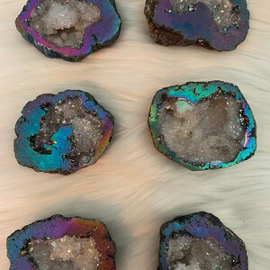 May include: Six iridescent agate geode slices with a white crystal interior. The geodes are various shapes and sizes and have a dark gray exterior with a rainbow sheen.