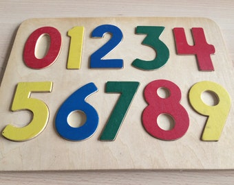 May include: A wooden puzzle board with colourful numbers 0 through 9. The numbers are painted red, yellow, blue, and green.