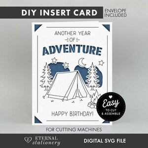May include: A white DIY insert card featuring a blue cutout design of a tent, pine trees, stars, and a crescent moon. The text reads ANOTHER YEAR OF ADVENTURE and HAPPY BIRTHDAY. A black circular badge states EASY TO CUT & ASSEMBLE.