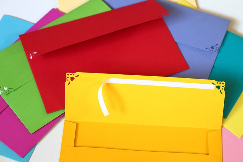 May include: A stack of colorful envelopes with decorative edges. The top envelope is yellow and open, revealing a white ribbon.