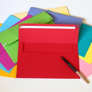 May include: A stack of colorful envelopes with decorative cutouts, a red envelope is open with a black pen on top of it.