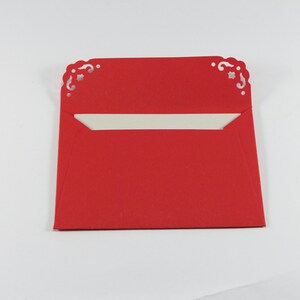 May include: A red envelope with a white interior and decorative cutouts on the top edge.