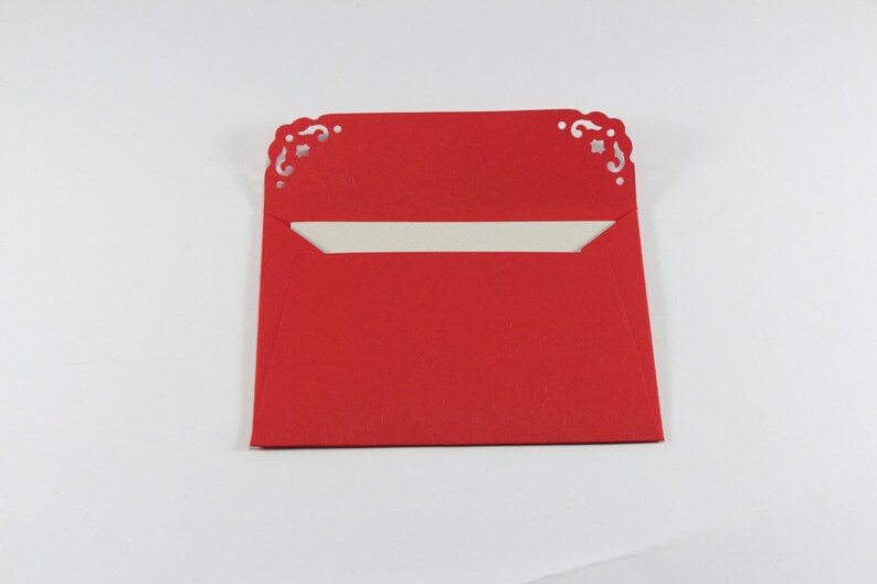 May include: A red envelope with a white interior and decorative cutouts on the top edge.