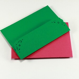 May include: Two folded cards, one green and one pink, with a decorative edge on the green card.