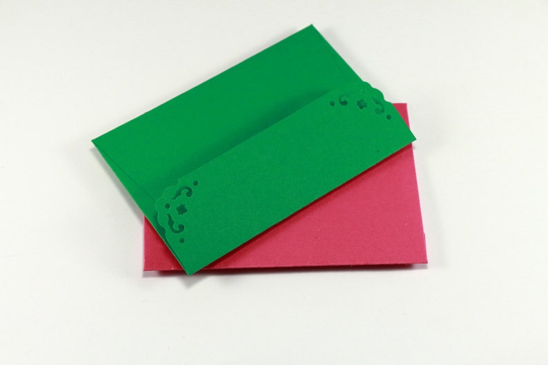May include: Two folded cards, one green and one pink, with a decorative edge on the green card.