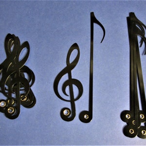 May include: Three black metal music note cutouts. The first is a treble clef, the second is a single note, and the third is a group of four notes.