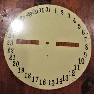 May include: A round, cream-colored metal disc with black numbers 1 through 31 around the edge. The numbers are evenly spaced and go clockwise. There are two rectangular cutouts on the disc, one on each side of the center.