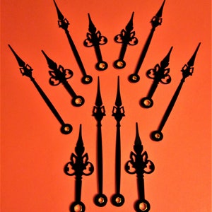 May include: A set of ten black clock hands with gold accents. The hands are arranged in a fan shape on a bright orange background.