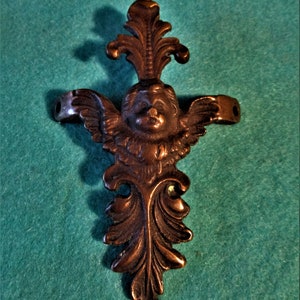 Op de afbeelding: Een bronzen cherub met vleugels en een bloemmotief. De cherub houdt een rol in zijn handen.