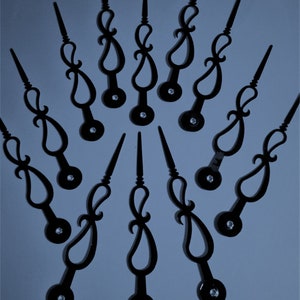 May include: A set of twelve black clock hands with a decorative design. The hands are arranged in a circle on a light blue background.