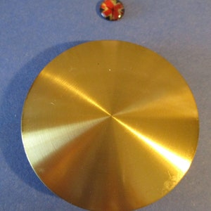 May include: A round, gold-colored metal disc with a brushed finish. The disc has a slight indentation in the center.
