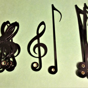 May include: A set of black metal music note cutouts. The set includes a treble clef, a bass clef, and a musical note. The cutouts are attached to a green background.