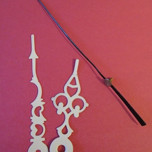 Puede incluir: Un juego de agujas de reloj, que incluye una aguja de hora larga negra y dos agujas decorativas blancas. Las agujas están sobre un fondo rojo.