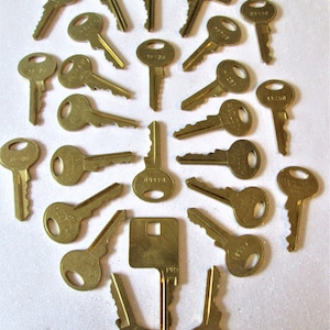 May include: A collection of 20 gold-toned keys with various numbers and letters engraved on them. The keys are arranged in a circular pattern on a white surface.