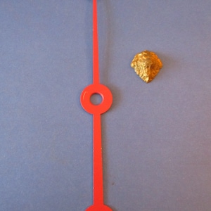 May include: A red clock hand with two circular holes and a crescent-shaped end. The hand is on a blue background.
