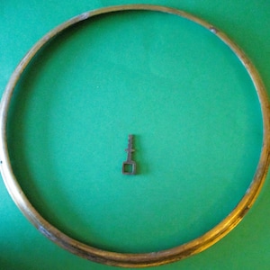 May include: A brass ring with a small, metal key on a green surface.