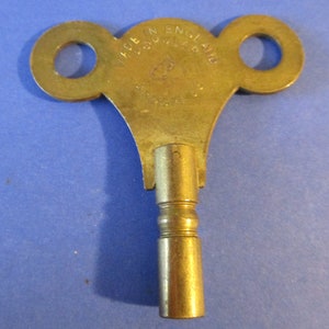 May include: A brass winding key with two loops on the top and the text "MADE IN ENGLAND POPULAR" on the front.
