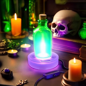 May include: A green glass bottle with a cork stopper sits on a purple light-up base. The bottle is filled with a glowing blue liquid. The base has a switch on the cord. The bottle is surrounded by candles and other decorative items.