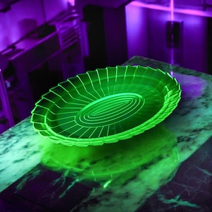 May include: A green glass plate with a fluted edge and a concentric circle design. The plate is illuminated with a purple light, creating a vibrant glow.