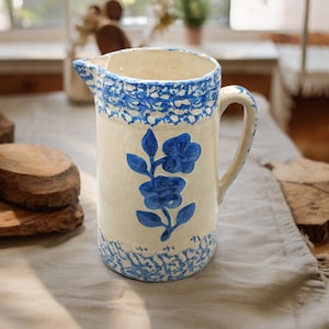 May include: A white ceramic pitcher with a blue floral design and a speckled blue glaze. The pitcher has a handle and a spout.