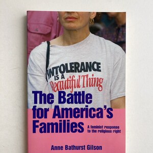May include: Book cover with a pink background and the title "The Battle for America's Families: A feminist response to the religious right" by Anne Bathurst Gilson. The cover features a person wearing a white t-shirt with the text "Intolerance is a beautiful thing" printed on it.