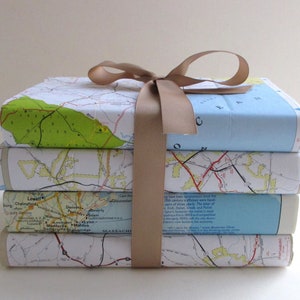 May include: A stack of four books wrapped in a brown ribbon. The books are covered in vintage maps of the United States. The maps are in shades of blue, green, and brown.