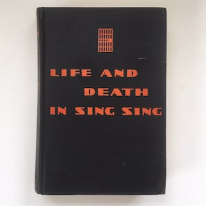 May include: A black book with the title "Life and Death in Sing Sing" printed in orange on the cover. A small orange illustration of a prison cell door is above the title.