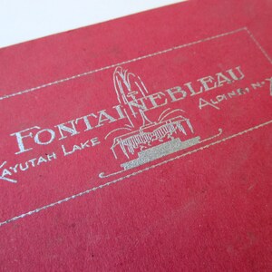 May include: A red card with silver lettering that reads "Fontainebleau, Kayutah Lake, Alpine, N.Y.". The card features a silver illustration of a fountain.