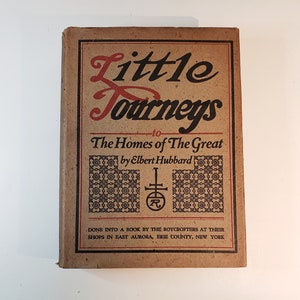 May include: A brown book titled "Little Journeys to The Homes of The Great" by Elbert Hubbard. The book is decorated with a black and white pattern and a red and black logo.