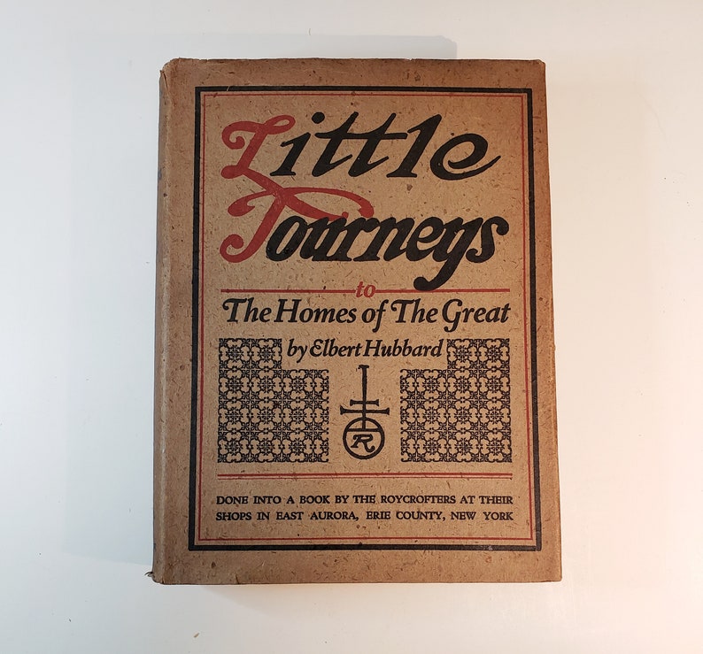 May include: A brown book titled "Little Journeys to The Homes of The Great" by Elbert Hubbard. The book is decorated with a black and white pattern and a red and black logo.
