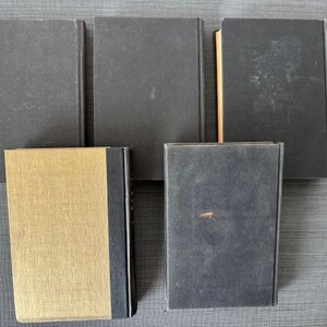 May include: A collection of five hardcover books. Four books have dark gray covers, while the fifth book has a gold cover with a black spine. The books are arranged on a gray surface.