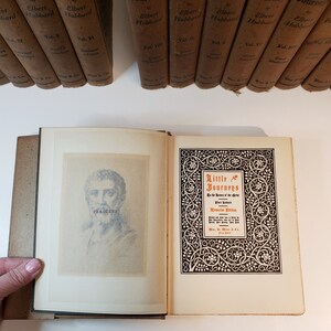 May include: An open book with a black and white illustration of Pericles on the left page and a title page for "Little Journeys to the Homes of Great Men" by Elbert Hubbard on the right page. The title page has a decorative border with a floral design.