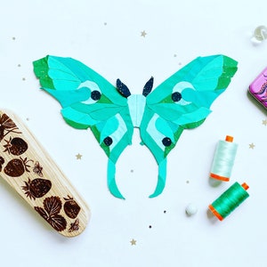 May include: A green and black paper butterfly with a detailed design. The butterfly is surrounded by small white stars and blue and white marbles. There is also a small pink box with a black octopus design.