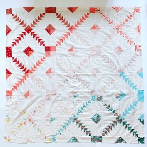 Peut inclure: Une courtepointe blanche avec un motif de patchwork composé de carrés de tissu rouge, rose, bleu et vert. La courtepointe est composée de différentes formes géométriques et de motifs.