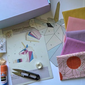 以下が含まれることがあります： Unicorn Dreamsのペーパーピーシングパターン、マスタード、ピンク、ラベンダー、花柄の布地、糸用バーム、スティックのり、金属製ボビン、黒い糸切りハサミが入ったクラフトキット。