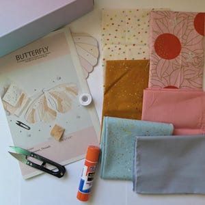 May include: A craft kit with fabric, scissors, glue, and a sewing pattern. The pattern is titled "BUTTERFLY" and features a butterfly design. Fabric pieces include star, floral, and solid patterns in various colours like pink, gold, and blue.