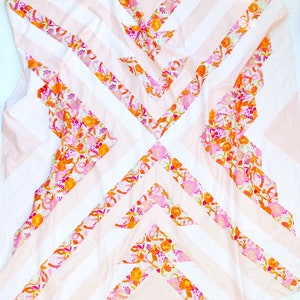 Pode incluir: Uma colcha rosa e branca com um padrão geométrico de listras laranja, rosa e brancas. A colcha é feita de tecido com estampa floral.