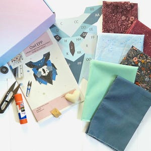 Könnte beinhalten: Ein Bastelset mit einem Eulen-Design, das Stoffstücke in verschiedenen Farben, ein Muster, eine Schere, Klebstoff und einen herzförmigen Gegenstand enthält. Das Set enthält eine Box mit einem rosa-blauen Farbverlauf und dem Text "Owl EPP".