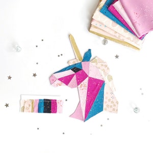 May include: A pink, blue, and gold geometric unicorn head made from fabric scraps. The unicorn is on a white background with silver glitter stars.