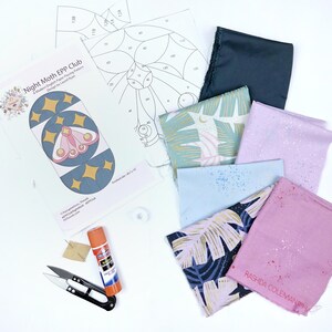 Könnte beinhalten: Ein Bastelprojekt-Layout mit einem "Night Moth EPP Club" Muster, Stoffresten, einer Schere, einem Klebestift und einer Nadel. Die Stoffstücke sind in verschiedenen Farben und Mustern gehalten, darunter dunkelblauer, hellblauer und rosa Stoff. Das Muster enthält eine Mottenillustration.