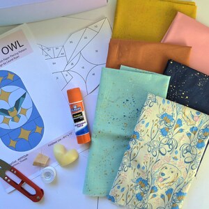 May include: A collection of quilting supplies including fabric scraps in various colors, paper piecing patterns, a glue stick, scissors, and a heart-shaped wax melt. The fabric includes a print with a dog and floral design.