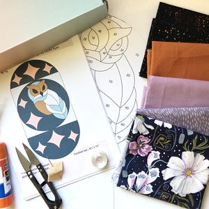 May include: A craft kit containing a printed owl pattern, a black and white line drawing template, five folded fabric swatches in black, rust, lavender, gray, and floral print, a glue stick, metal snips, a thread balm packet, and a bobbin.