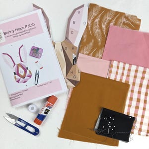 Könnte beinhalten: Ein Bastelset für ein modernes englisches Papier-Piecing-Projekt mit einem Hasenmuster. Das Set enthält Stoffmuster, eine Vorlage, eine Schere, einen Klebestift und Faden. Die fertige Größe beträgt 17,78 cm x 25,4 cm.