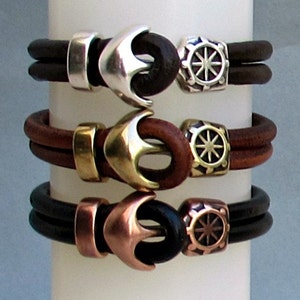 May include: Three leather bracelets with anchor and compass charms. The bracelets are brown, black, and brown with silver, brass, and copper accents.