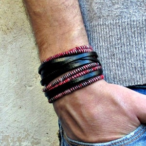 Puede incluir: Un brazalete de capas con correas de cuero negro y cordón trenzado rojo y blanco.