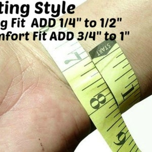 May include: A yellow measuring tape wrapped around a wrist to demonstrate how to measure for a snug or comfort fit. The text on the tape reads "START". The text above the tape reads "Fitting Style", "Snug Fit ADD 1/4" to 1/2"", and "Comfort Fit ADD 3/4" to 1"".