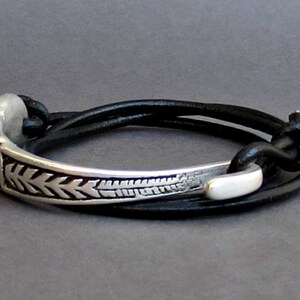 May include: A silver bracelet with a decorative design and a black leather strap. The strap is adjustable and can be worn in multiple ways.